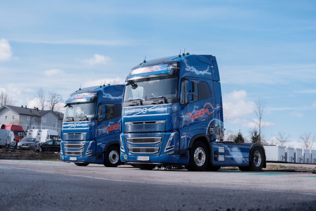 Zwei LKW von VEGA International stehen auf einem Parkplatz